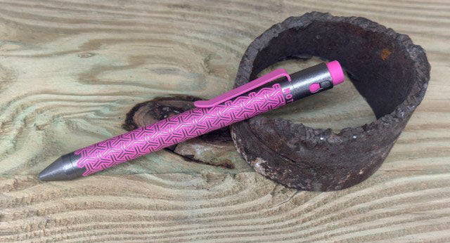 Titanium Custom Cerakote Pen in pink with diamond grip pattern next to wooden bowl - NTI tactical pen